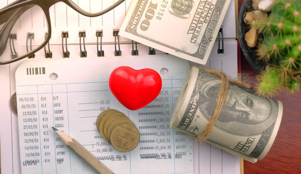 Cash, coins, pencil and red heart rest on paper log of bills paid | Best emergency loans.