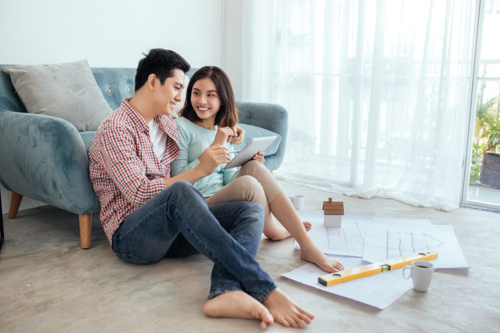 Couple sits on the floor with paper renovation plans as they apply for a loan on tablet | How to get a home repair loan